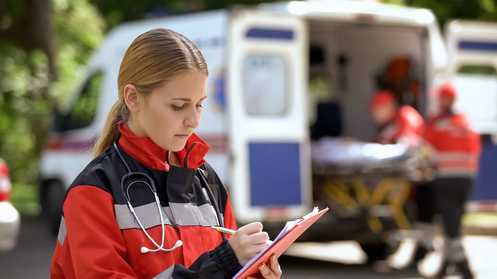 Женщина-врач ведет медицинские записи, команда скорой помощи перевозит пациента
 - Фото, изображение