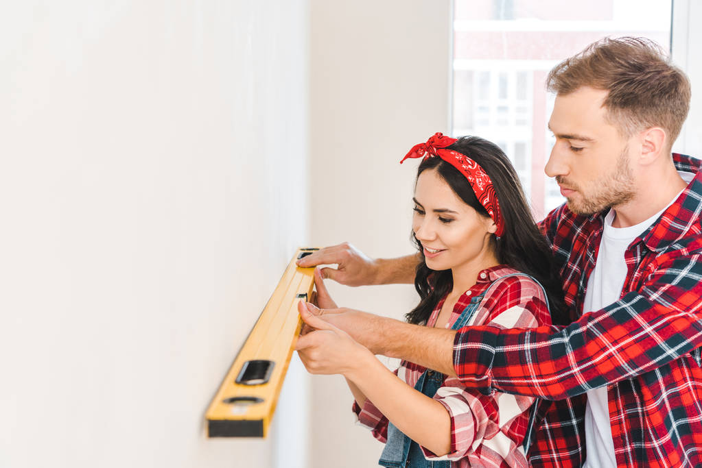 cheerful couple holding measuring level near wall at home - Photo, Image