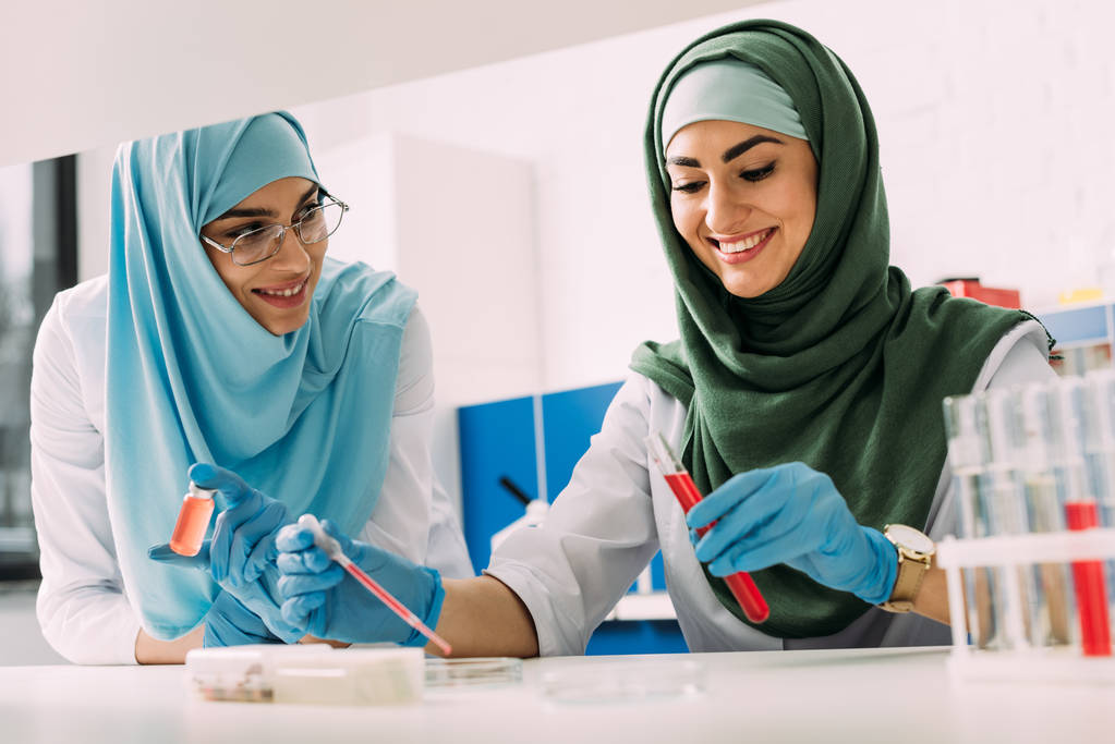 scientifiques musulmanes souriantes en hijab avec éprouvette et pipette lors d'une expérience en laboratoire chimique
 - Photo, image