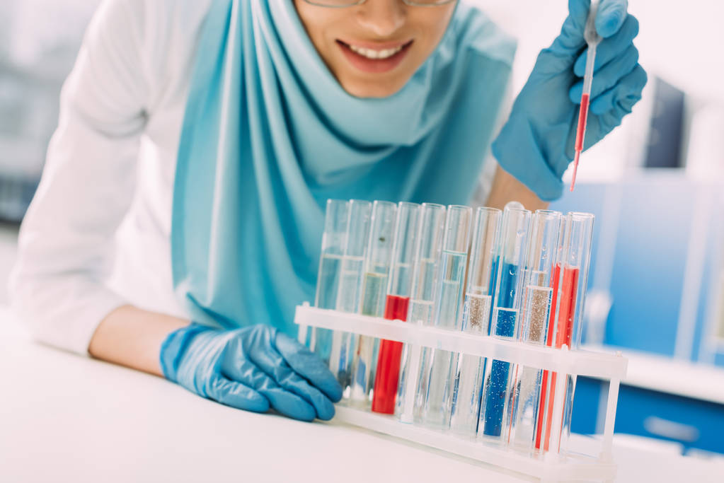 обрезанный вид улыбающейся мусульманки-ученого, добавляющей кровь в пробирку в лаборатории
 - Фото, изображение
