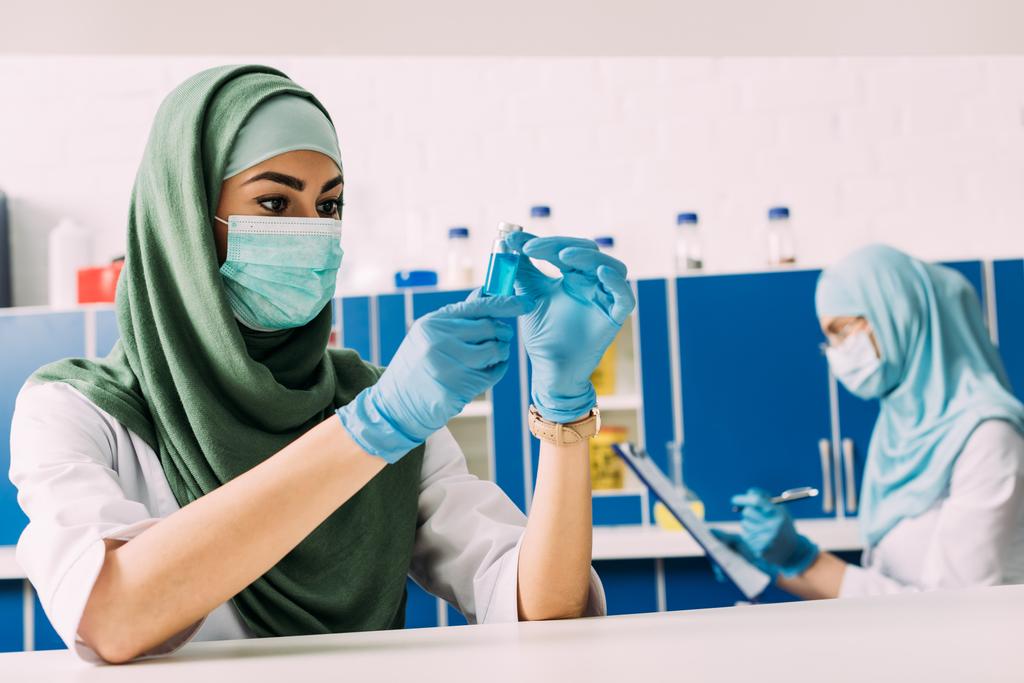 női muzulmán tudós gazdaság kémcsőben folyékony, a kémiai laboratóriumi kísérlet során orvosi maszkot - Fotó, kép