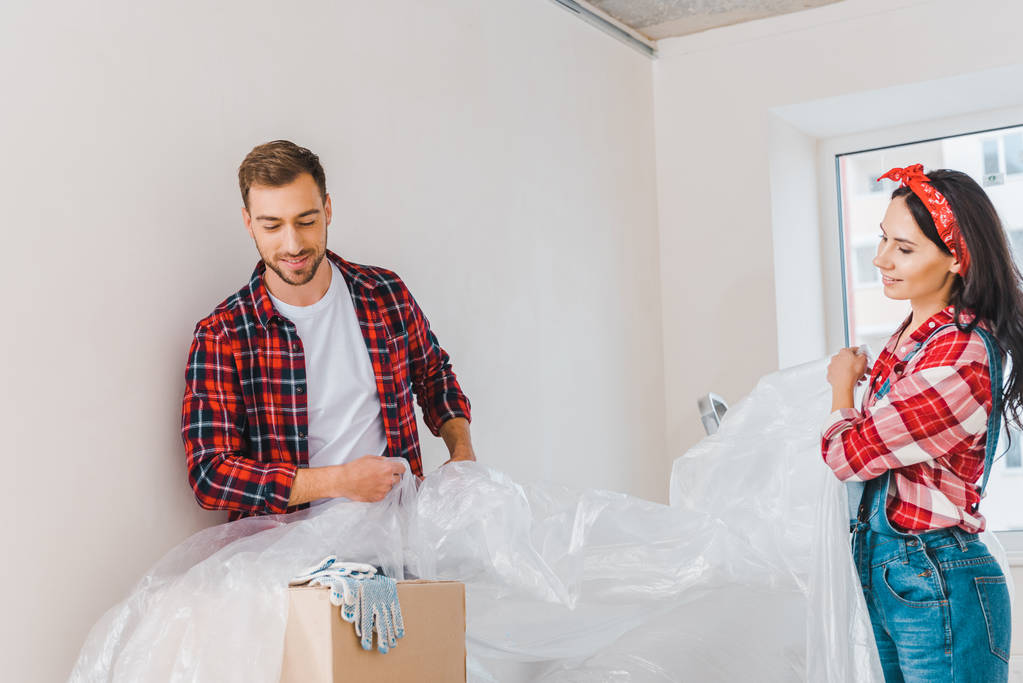 hombre y mujer alegre cubriendo cajas con polietileno en casa
 - Foto, imagen