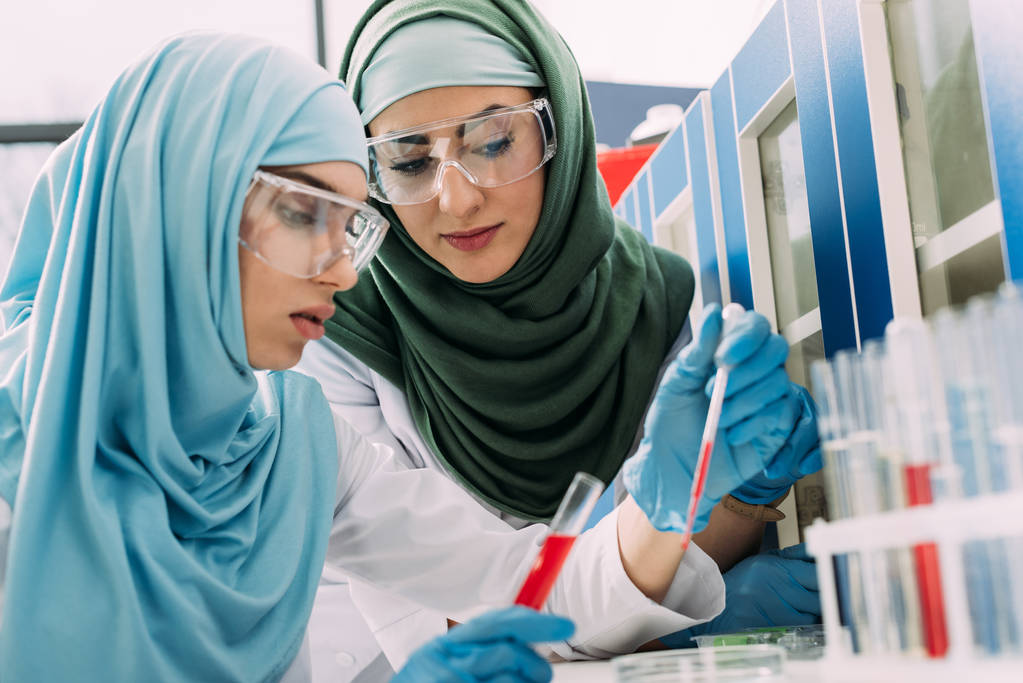 científicas musulmanas en gafas protectoras con pipeta y tubo de ensayo durante el experimento en laboratorio químico
 - Foto, Imagen