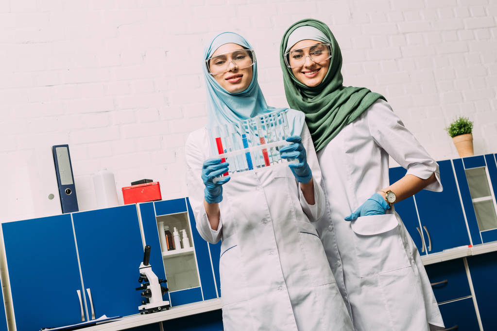 female muslim scientists with test tubes looking at camera during experiment in chemical lab - Photo, Image