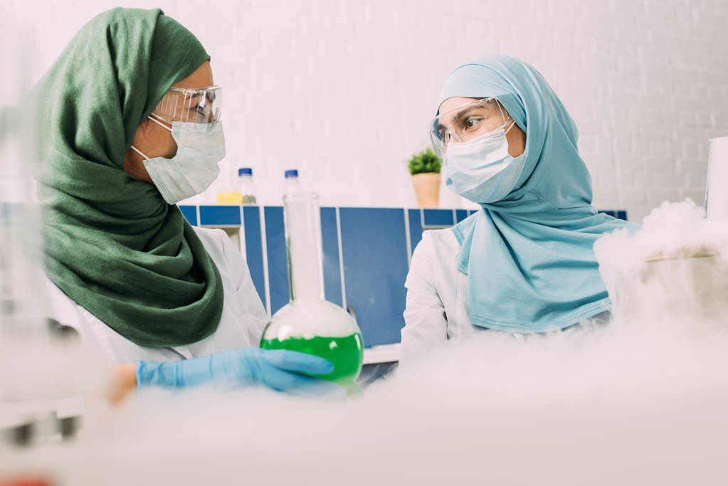 scientifiques musulmanes avec fiole regardant les uns les autres tout en expérimentant avec de la glace sèche en laboratoire chimique
 - Photo, image