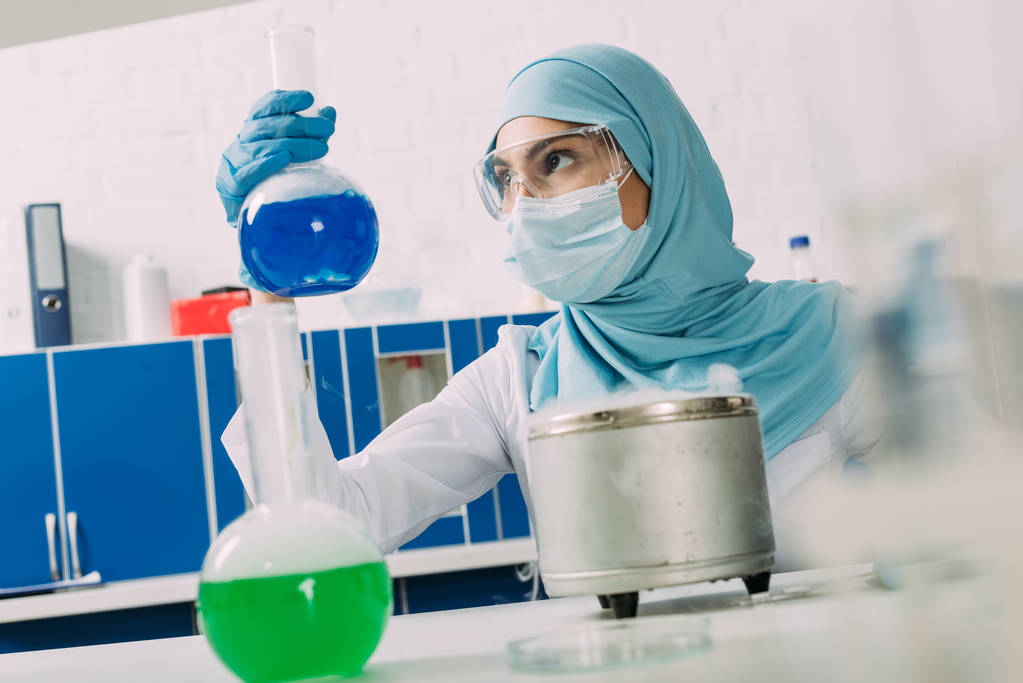 cientista muçulmano fêmea olhando para o frasco durante o experimento em laboratório químico
 - Foto, Imagem