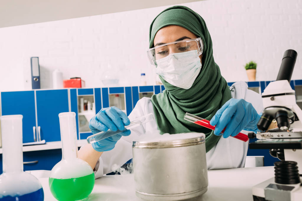 naispuolinen muslimitutkija, jolla on koeputkia kuivajäällä potin päällä laboratoriossa tehtävän kokeen aikana
 - Valokuva, kuva