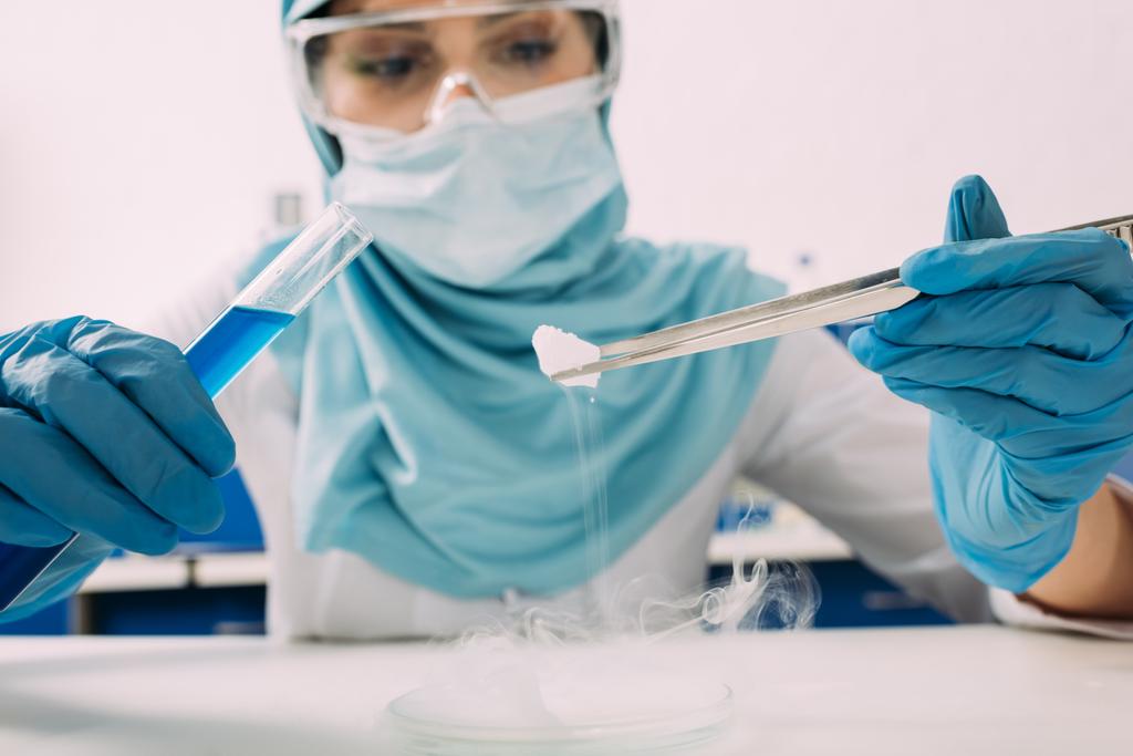 oříznutý pohled na ženské muslimské vědce drží zkumavky s pinzetou a experimentování s suchým ledem v laboratoři - Fotografie, Obrázek