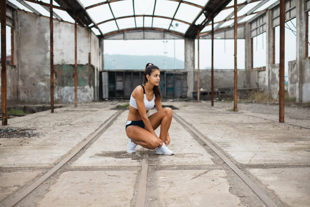 Młodych kobiet sportowiec szykując się na zewnątrz kolejny trening. Sportowcy girl sznurowanie obuwia w starych ruinach przemysłowe. - Zdjęcie, obraz