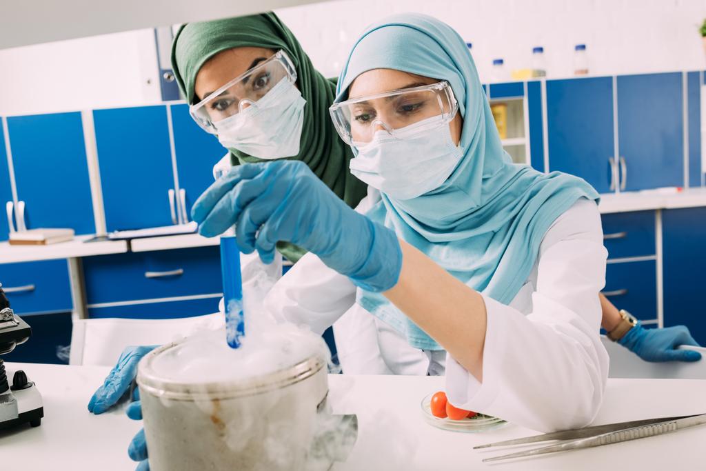 kobiet muzułmańskich naukowców w gogle gospodarstwa odczynnika na suchy lód podczas eksperyment w laboratorium chemicznym - Zdjęcie, obraz