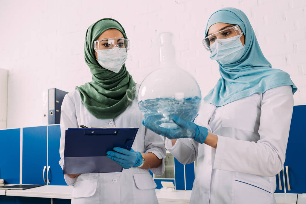 female muslim scientists holding clipboard and flask wth liquid in chemical laboratory - Photo, Image