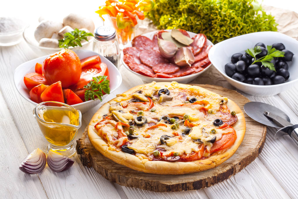 leckere italienische Pizza und Zutaten auf dem weißen Holztisch serviert - Foto, Bild