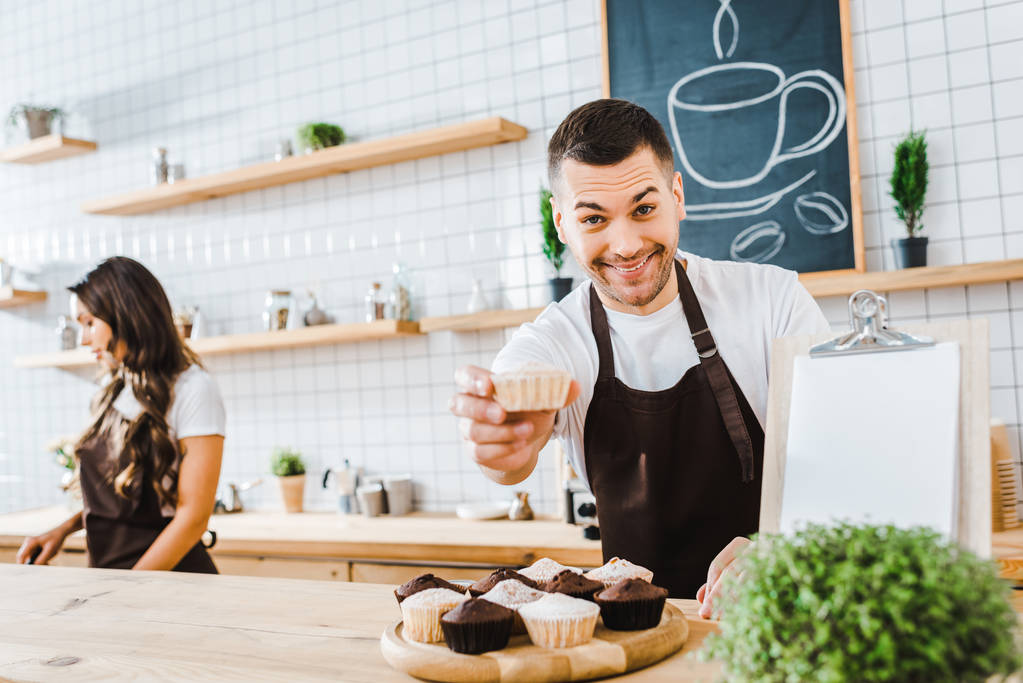 messa a fuoco selettiva di bello barista dando cupcake wile attraente bruna cassiere lavorando in caffetteria
 - Foto, immagini