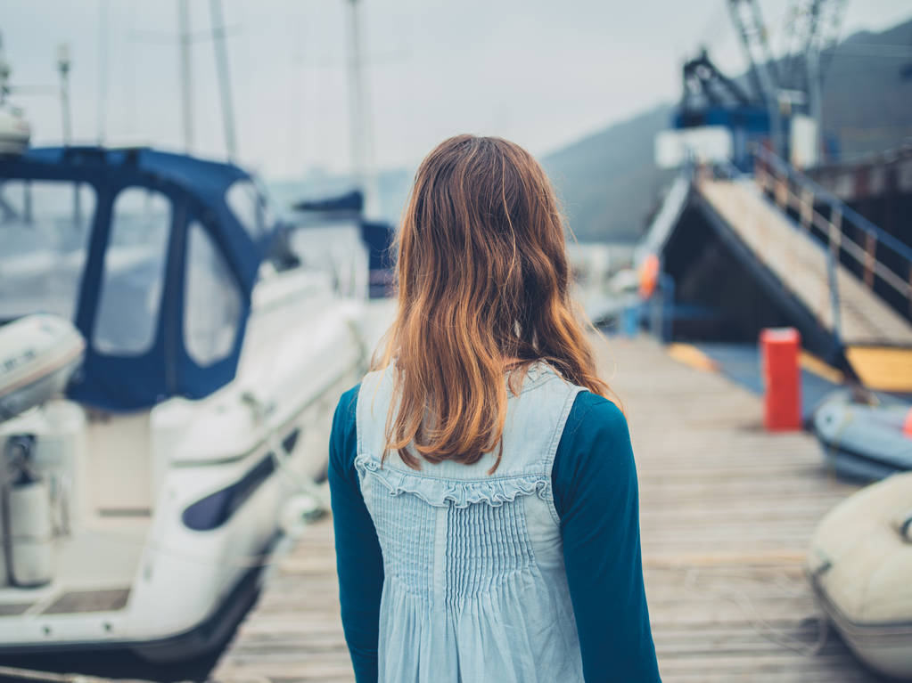 Una joven está caminando en un puerto deportivo con barcos
 - Foto, imagen