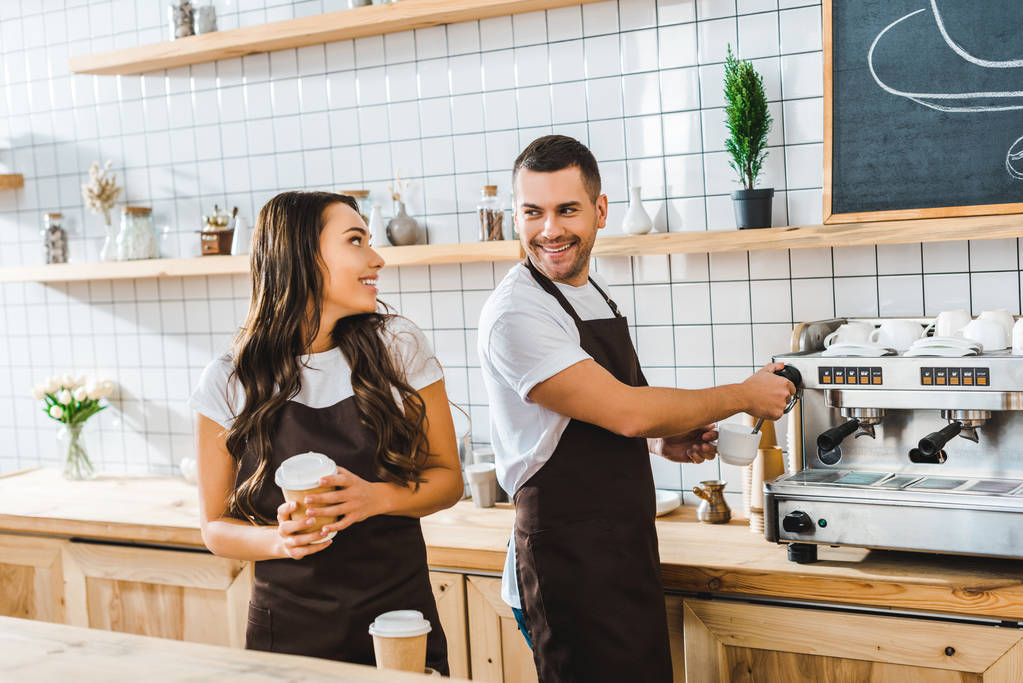 przystojny barista do parzenia kawy i atrakcyjny brunetka Kasjer trzymając kubek papierowy w coffee house - Zdjęcie, obraz