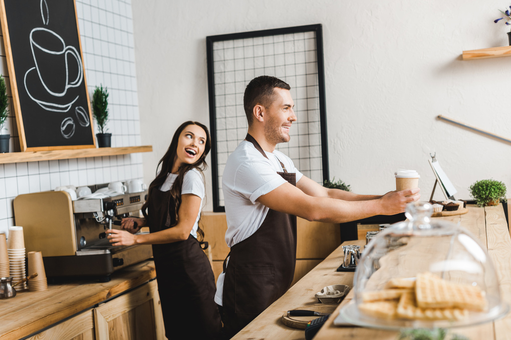przystojny Kasjer dając papieru kubki wile atrakcyjne barista kawy i uśmiechając się za kontuarem w coffee house - Zdjęcie, obraz