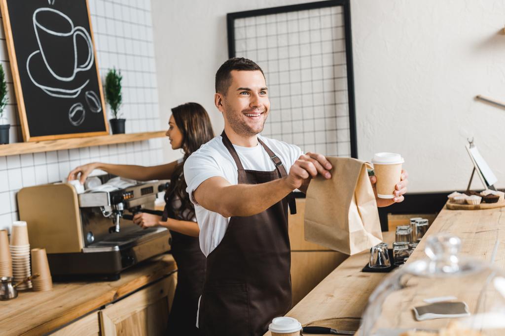 komea kassanhoitaja antaa paperimuki ja laukku wile barista tehdä kahvia tiskin takana kahvilassa
 - Valokuva, kuva