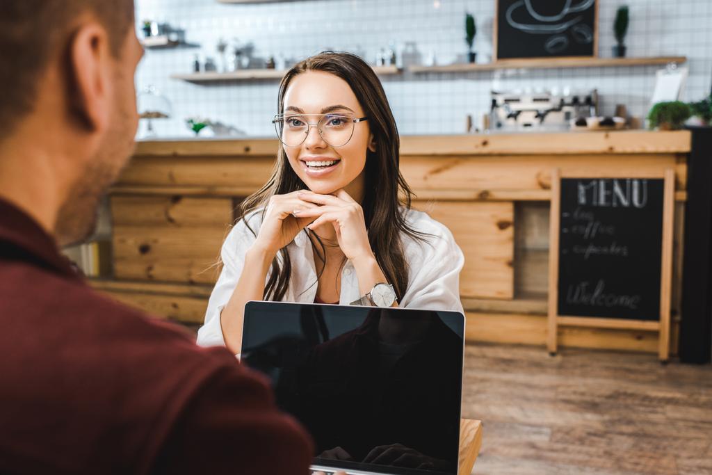 selectieve aandacht van aantrekkelijke vrouw zittend aan tafel en praat met de man met de laptop in koffiehuis - Foto, afbeelding