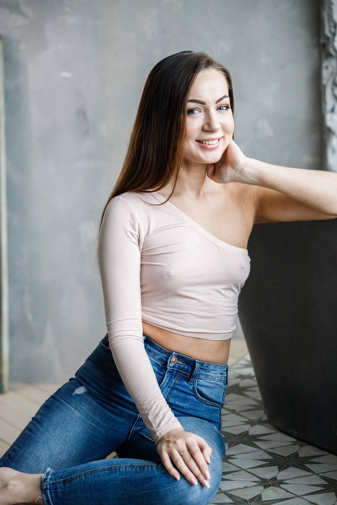Portret pięknej młodej kobiety w dżinsach i beżowy t-shirt. Młody model siedzi na podłodze w luksusowe apartamenty wnętrze - Zdjęcie, obraz