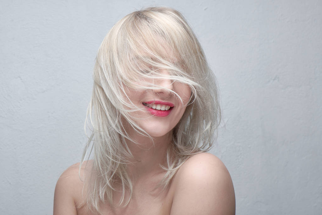 Портрет молодой красивой улыбающейся блондинки с пухлыми красными губами и обнаженными плечами на белом фоне. Модная прическа
 - Фото, изображение