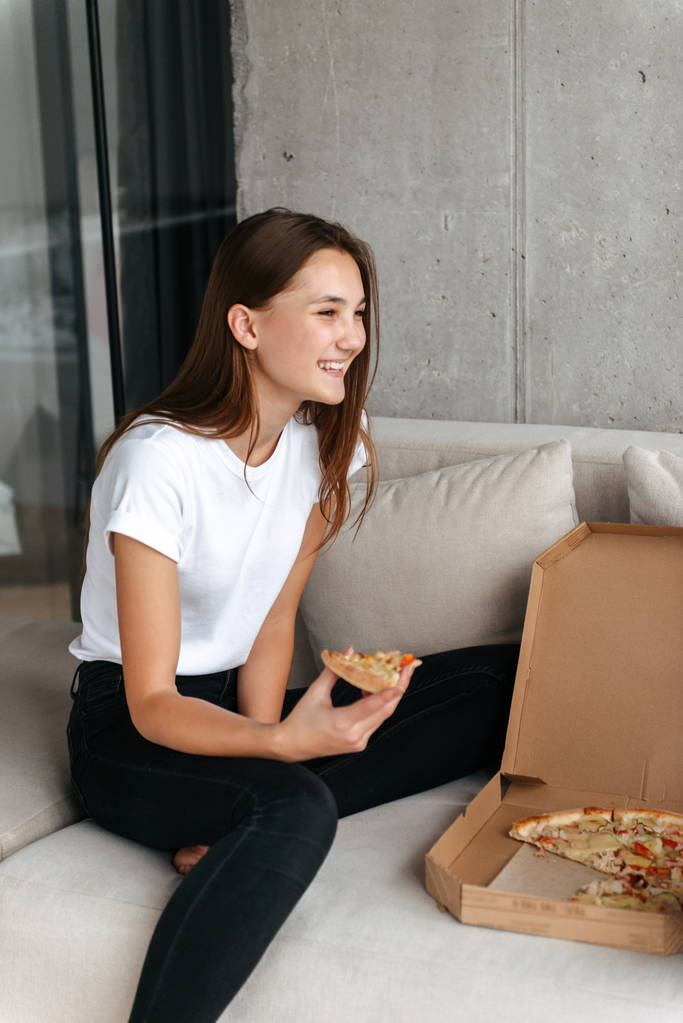 Boldog fiatal tizenéves lány egy kanapén pizzát eszik - Fotó, kép