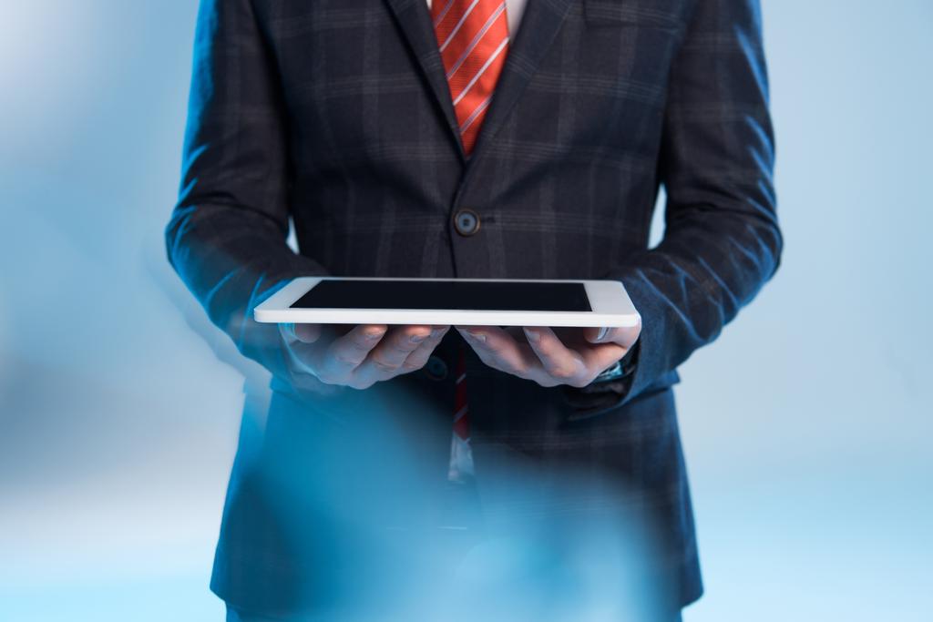 selective focus of businessman holding digital tablet on blue - Photo, Image