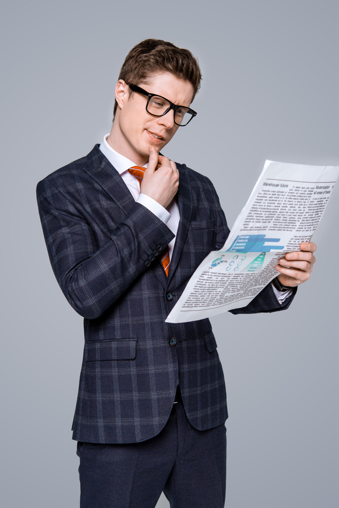 стильный молодой бизнесмен читает газету изолированы на серый
 - Фото, изображение