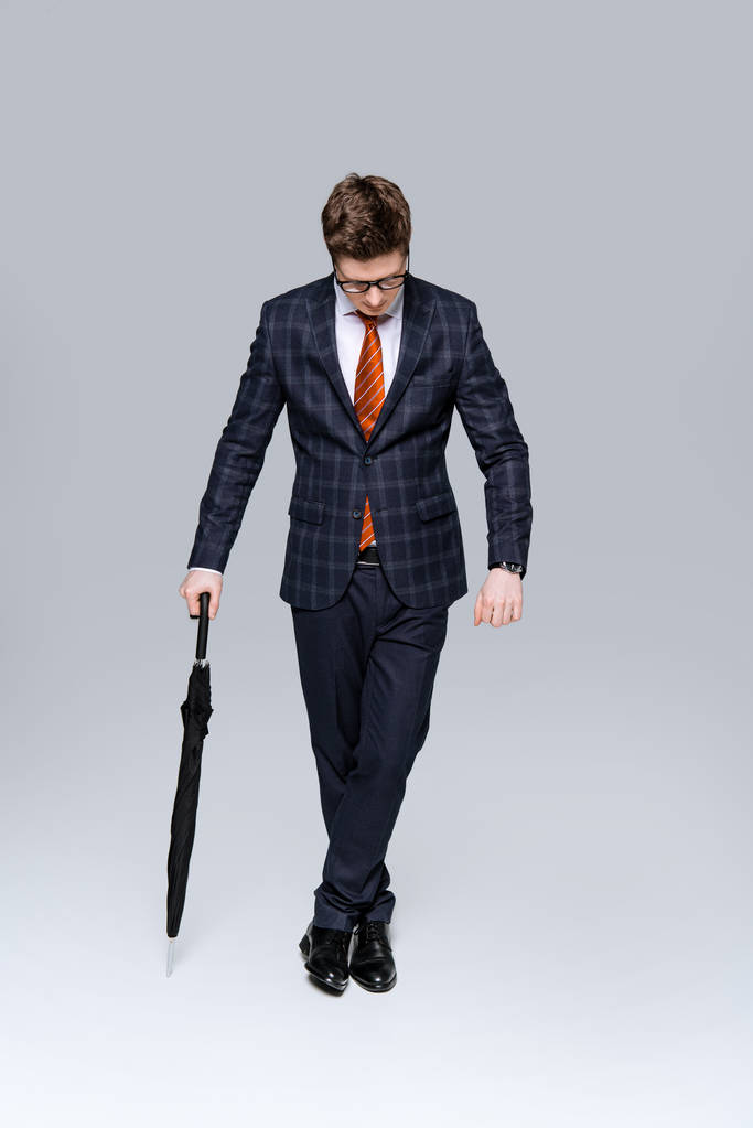 Stylischer Geschäftsmann im Anzug posiert mit Regenschirm auf Grau - Foto, Bild