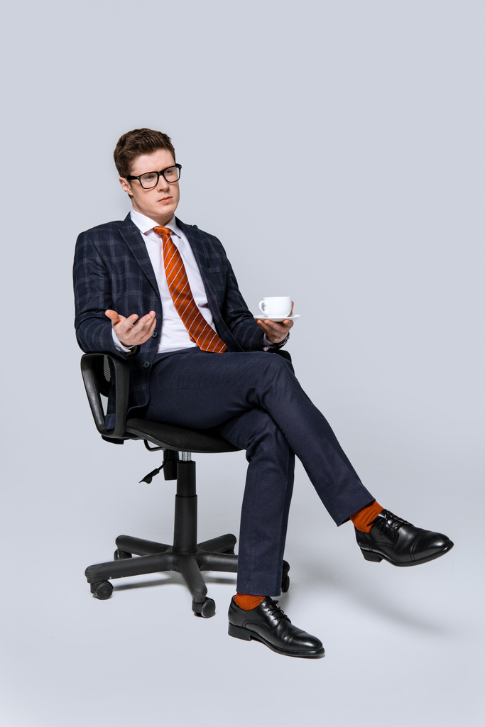 κομψό επιχειρηματία που κάθεται σε καρέκλα με φλιτζάνι καφέ σε γκρι - Φωτογραφία, εικόνα