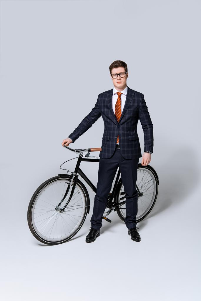 κομψό επιχειρηματία στο κοστούμι στέκεται με ποδήλατο σε γκρι  - Φωτογραφία, εικόνα