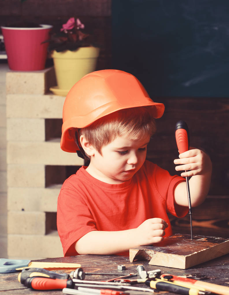 Boy play como construtor ou reparador, trabalhar com ferramentas. Rapaz de chapéu laranja ou capacete, fundo da sala de estudo. Conceito de infância. Criança sonhando com carreira futura em arquitetura ou construção
 - Foto, Imagem