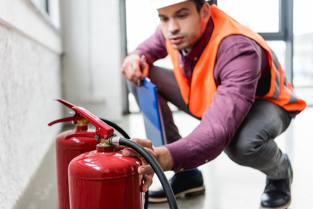 selective focus of red extinguishers near fireman in helmet holding clipboard - Photo, Image