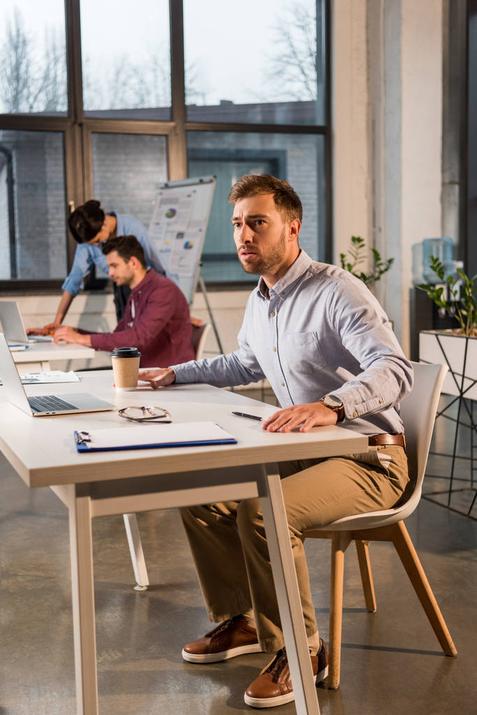 страшний бізнесмен сидить і тримає паперову чашку біля співробітників в офісі
 - Фото, зображення
