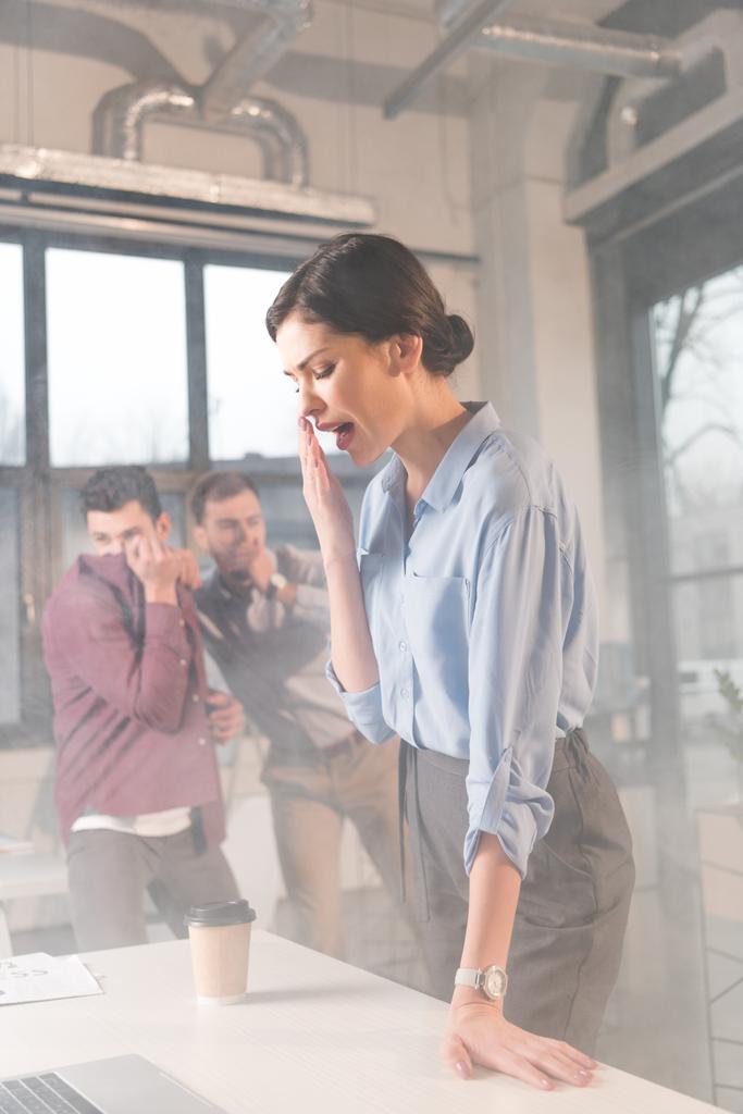 Geschäftsfrau steht mit offenem Mund neben Mitarbeitern im Büro und raucht - Foto, Bild