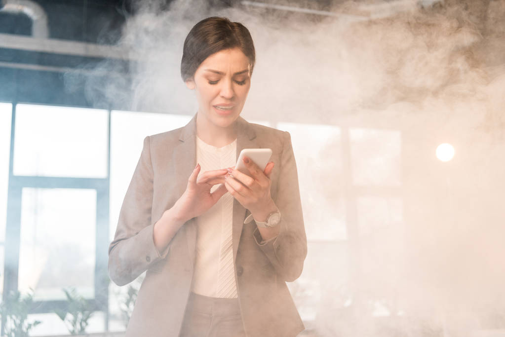 страшна бізнес-леді, дивлячись на смартфон в офісі з димом
 - Фото, зображення