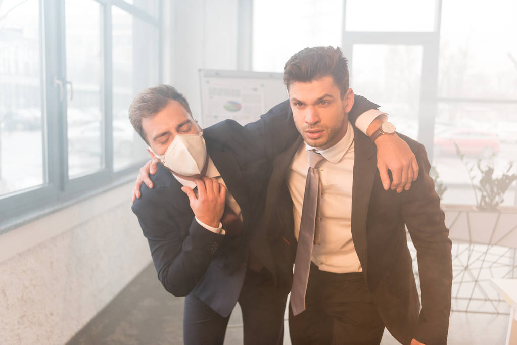 empresário aterrorizado em máscara de pé com colega de trabalho sério no escritório com fumaça
 - Foto, Imagem