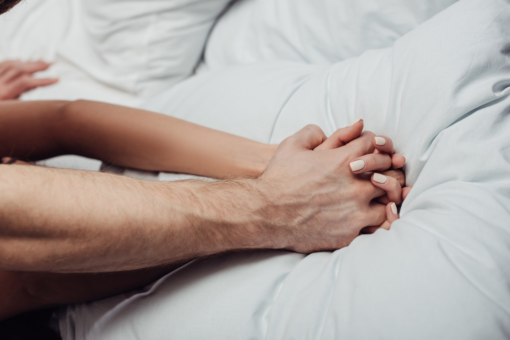 περικοπεί θέα ζευγάρι κρατώντας τα χέρια και ξαπλωμένη στο κρεβάτι στο σπίτι - Φωτογραφία, εικόνα
