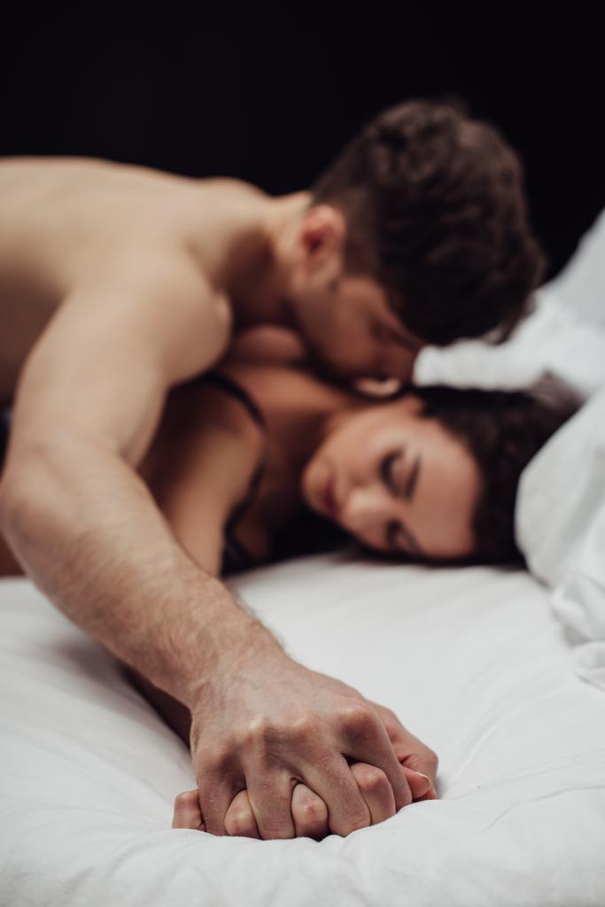 mladý pár leží v posteli a drželi se za ruce, samostatný na černém - Fotografie, Obrázek