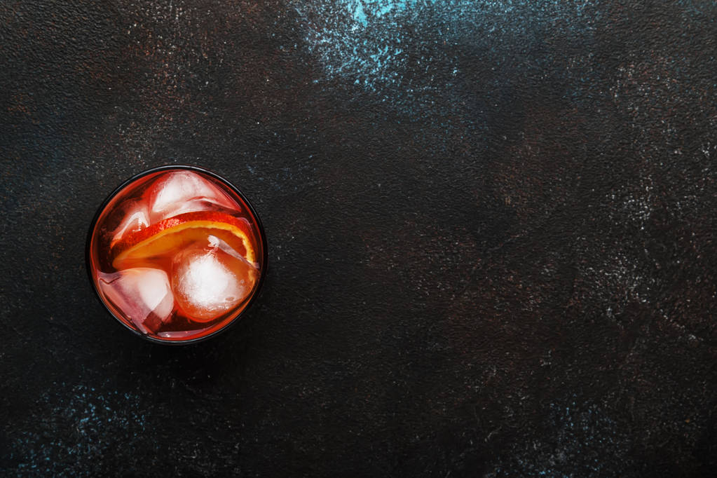 Cocktail alcoólico moderno Negroni com gim seco, vermute vermelho e vermelho amargo, laranja e cubos de gelo. Barra marrom contador de fundo, estilo minimalista, vista superior, lugar para texto
. - Foto, Imagem