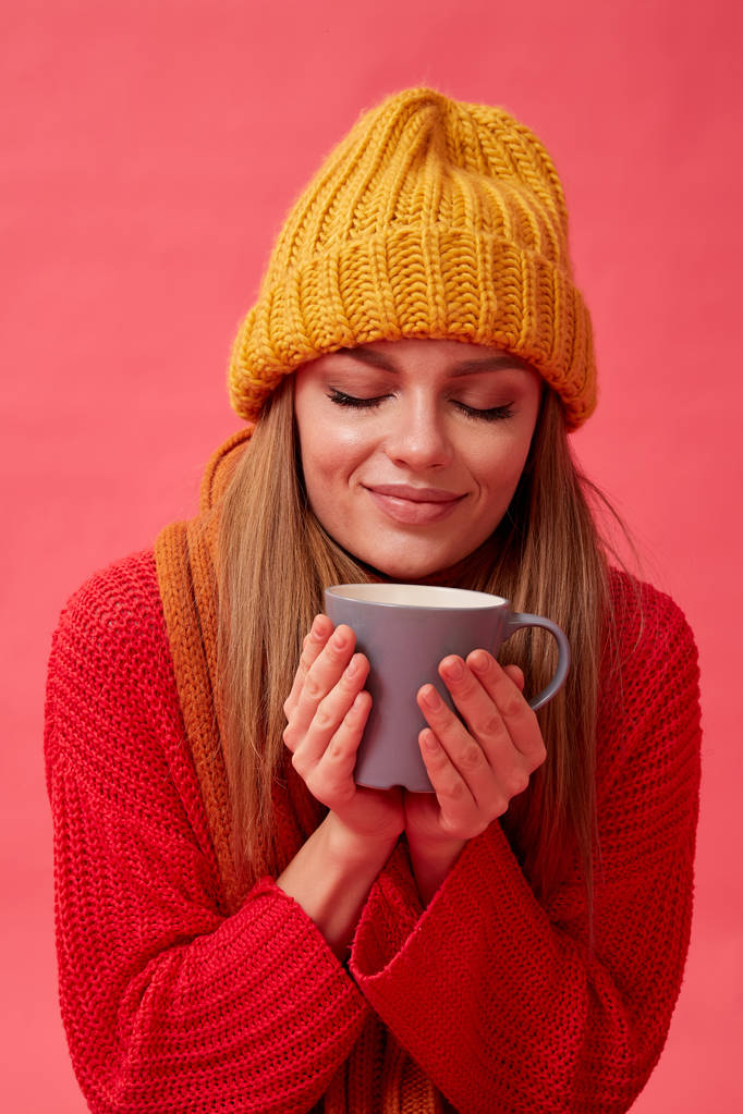 Hermosa adolescente en suéter cálido y acogedor con taza de bebida caliente. Fondo rojo. Estudio
 - Foto, imagen