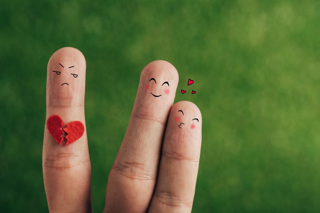 abgeschnittene Ansicht von Fingern als glückliches verliebtes Paar und drittes Rad mit gebrochenem Herzen auf Grün - Foto, Bild