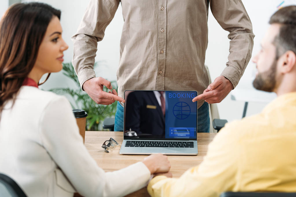 オフィスでカップルの近くでスクリーンの予約サイトでノート パソコンの指で指しているアドバイザーの選択と集中 - 写真・画像