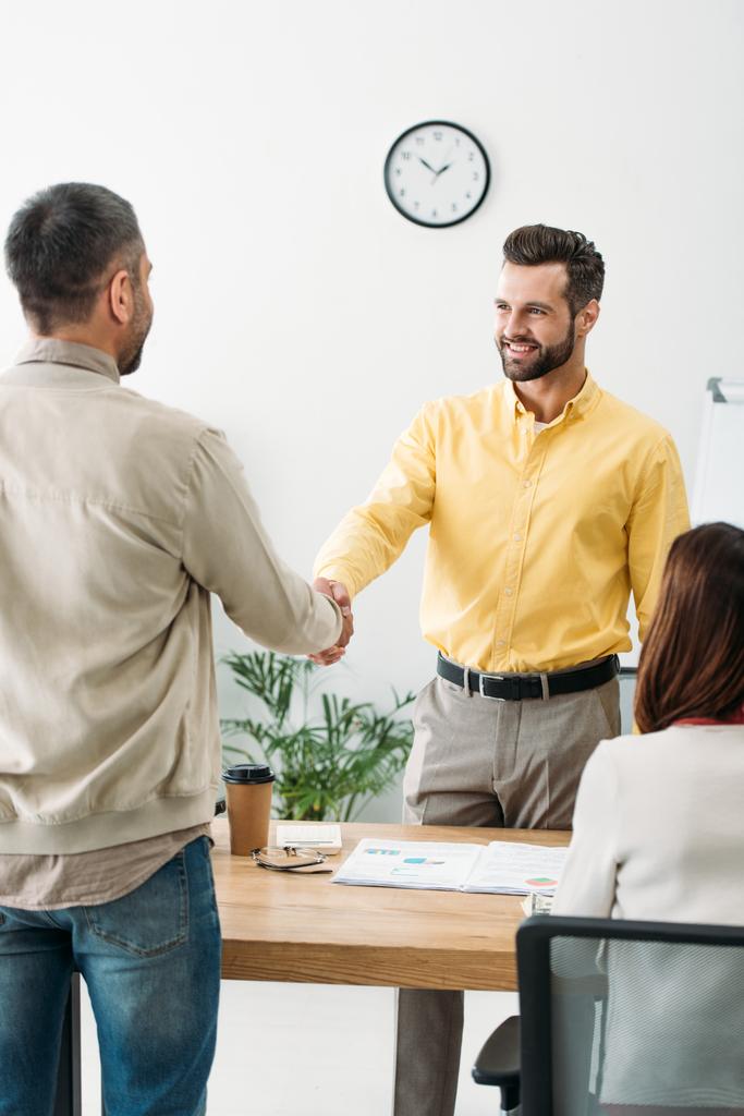 advisor and investor shaking hands over table wile woman sitting in office - Photo, Image