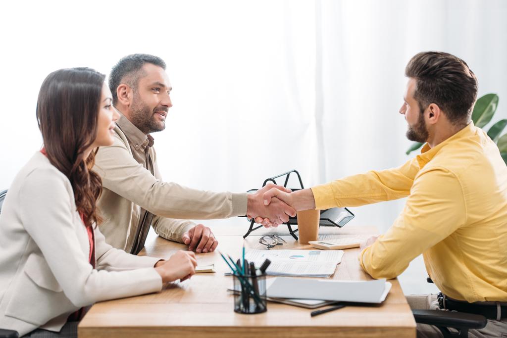 woman sitting at table wile advisor and investor shaking hands over table in office - Photo, Image