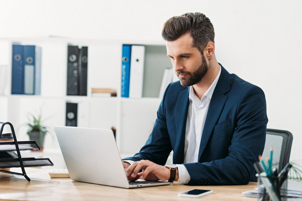 hombre de negocios en traje azul sentado en la mesa con el ordenador portátil y escribiendo en la oficina
 - Foto, imagen