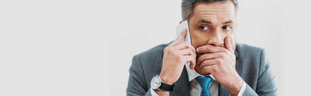 scered zakenman in grijs pak praten over smartphone geïsoleerd op wit - Foto, afbeelding