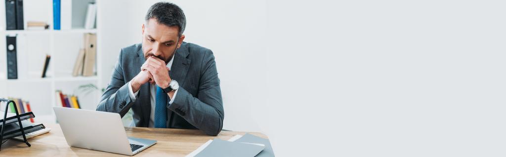 hombre de negocios guapo en traje gris sentado en la mesa con el ordenador portátil y pensando en la oficina
 - Foto, Imagen