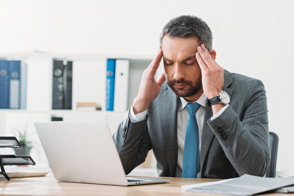 dizüstü bilgisayar ve ofis duygu baş ağrısı masada oturan yakışıklı işadamı - Fotoğraf, Görsel
