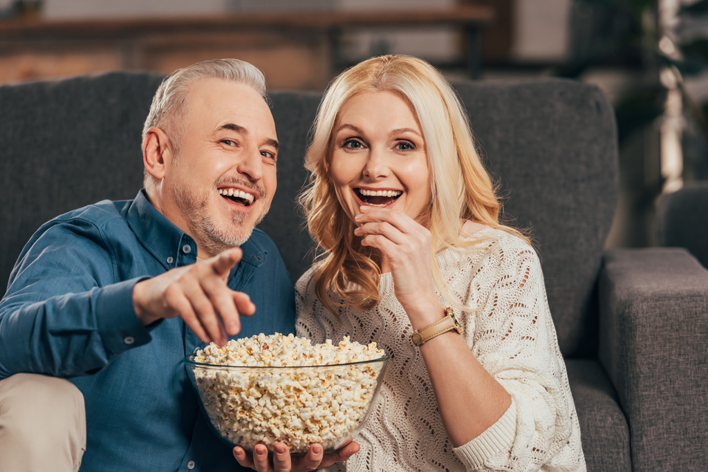 onnellinen mies osoittaa sormella pitäen kulhoon popcorn lähellä vaimo
 - Valokuva, kuva