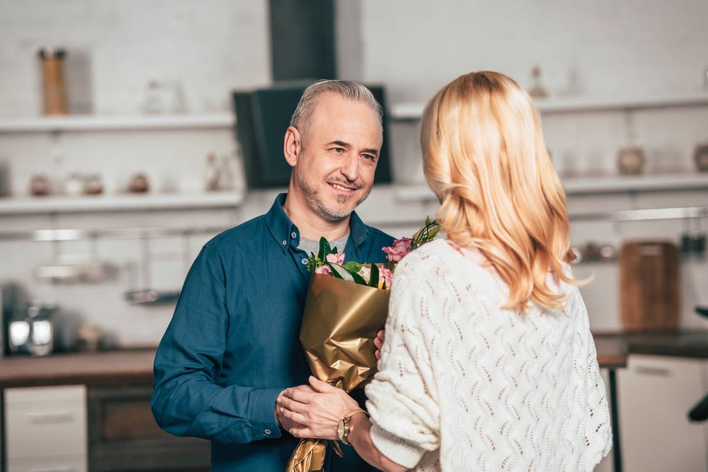 счастливый мужчина улыбается, давая цветы жене-блондинке
  - Фото, изображение